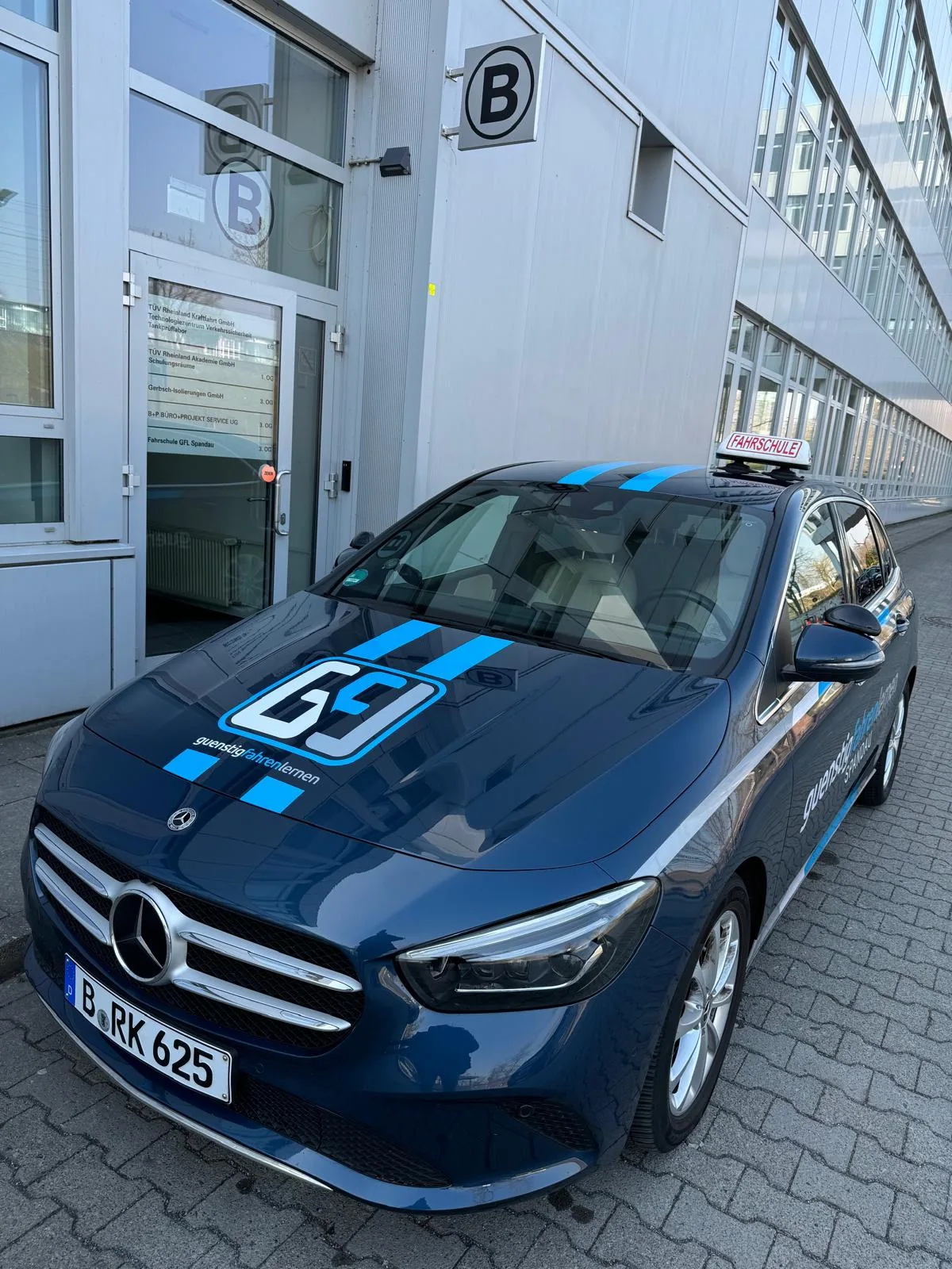 Fahrschulwagen der GFL Spandau vor dem Eingang des TÜV-Gebäudes